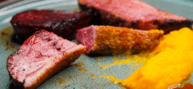 Sliced duck breast cooked to medium rare on a plate. With mashed yellow sweet potato