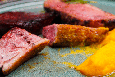 Sliced duck breast cooked to medium rare on a plate. With mashed yellow sweet potato