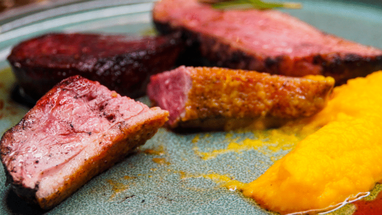 Sliced duck breast cooked to medium rare on a plate. With mashed yellow sweet potato