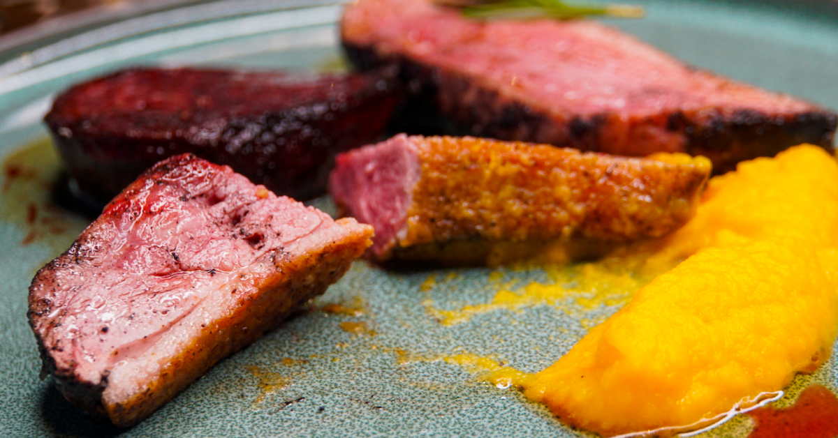 Sliced duck breast cooked to medium rare on a plate. With mashed yellow sweet potato