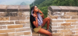 Woman sitting on the great wall of China, with hills and greenery behind her, seemingly enjoying the breath of fresh air.