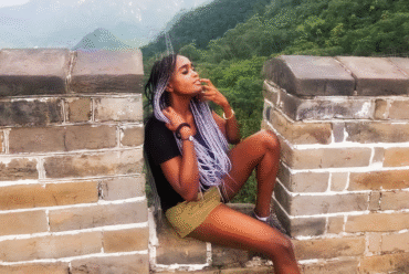 Woman sitting on the great wall of China, with hills and greenery behind her, seemingly enjoying the breath of fresh air.