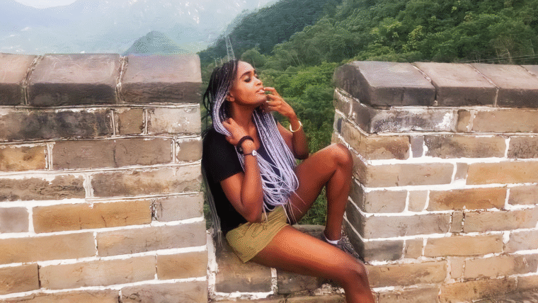 Woman sitting on the great wall of China, with hills and greenery behind her, seemingly enjoying the breath of fresh air.