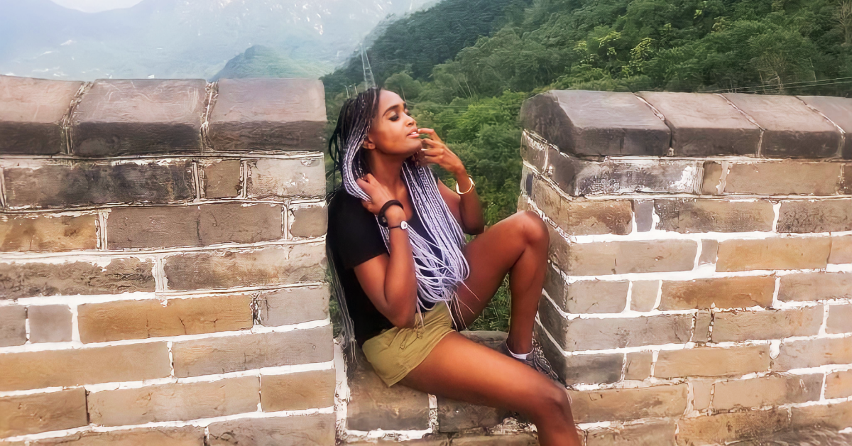 Woman sitting on the great wall of China, with hills and greenery behind her, seemingly enjoying the breath of fresh air.