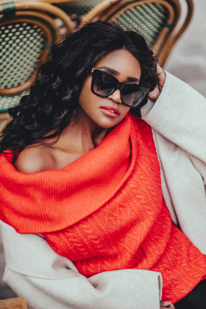 A woman in a red sweater, chic sunglasses, and curly brown hair, exudes style with a subtle touch
