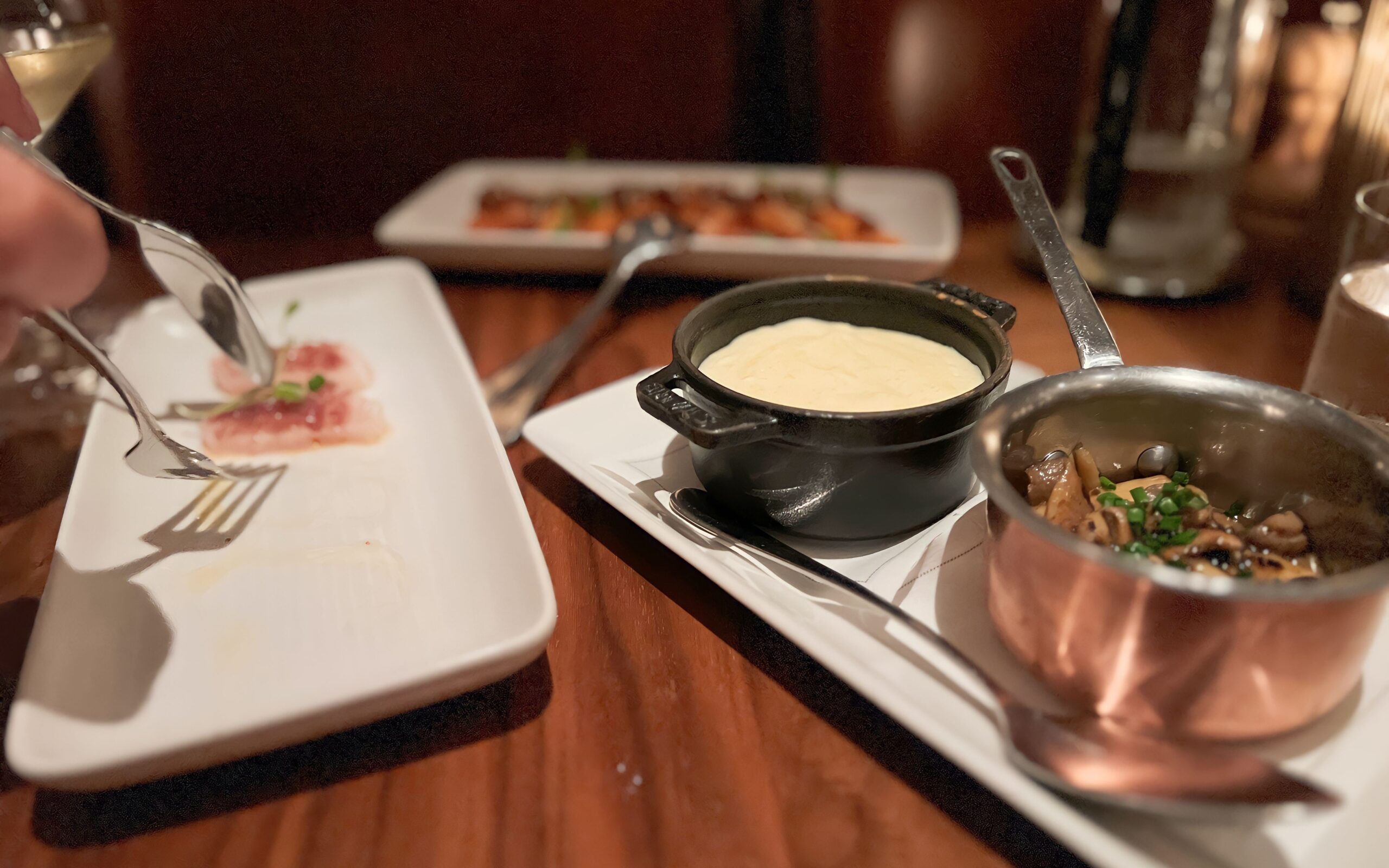 Mushroom in a copper pot next to polenta served in a black pot, next to two other starter dishes.