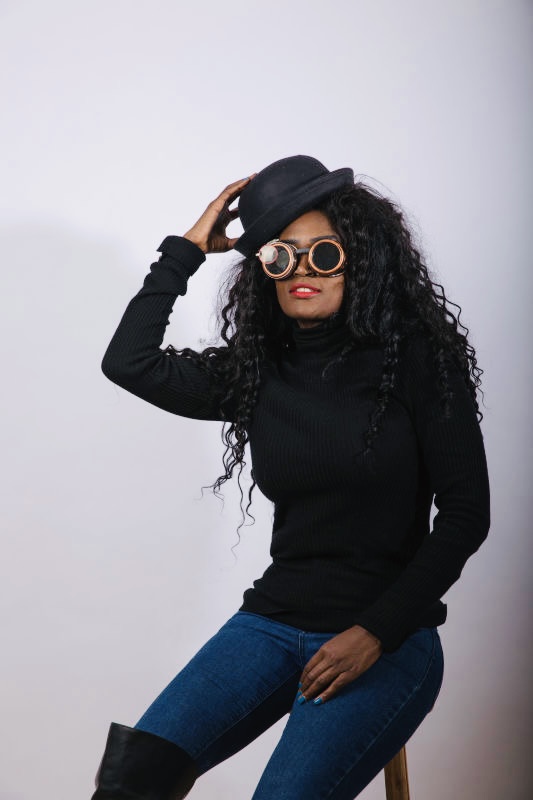 Fashion-forward woman in black turtleneck and blue jeans, accessorised with a black hat and unique round glasses, demonstrating personal style.
