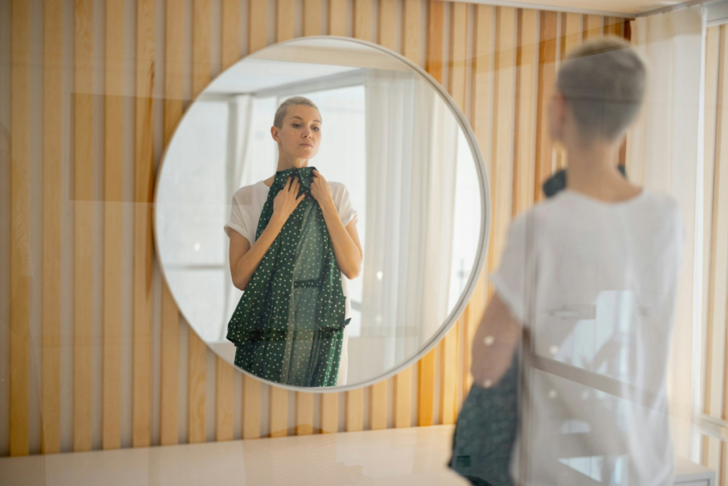 Woman in a fitting room trying on a dotted dress while shopping alone.