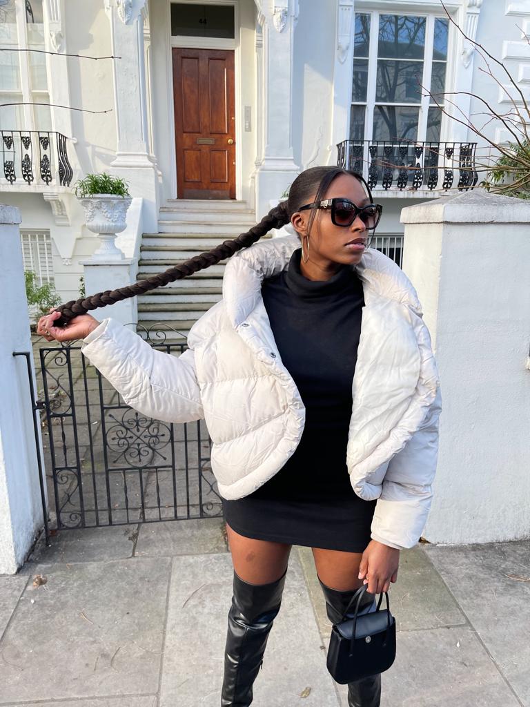 Chic woman donning a white quilted collared puffer jacket, paired with a stylish short black dress and over-the-knee boots for a fashion-forward winter look.