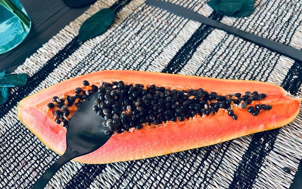 Papaya on the table. Black spoon scooping black seeds from an orange papaya