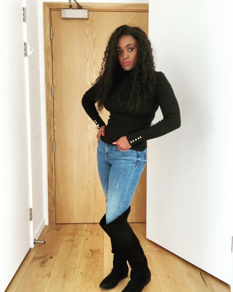 A woman poses in blue jeans and knee-high boots, effortlessly blending rugged charm with chic style, creating a versatile and timeless fashion statement.