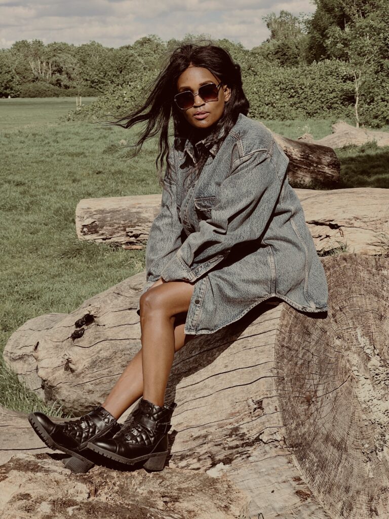 Stylish woman in a denim jacket, sitting on a rock, showcasing black ankle boots – a chic and casual outdoor fashion moment.