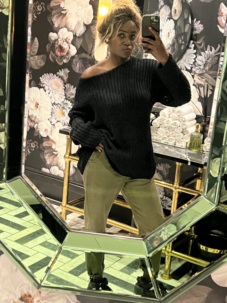 Woman wearing stylish green denim jeans and black top taking a selfie in bathroom