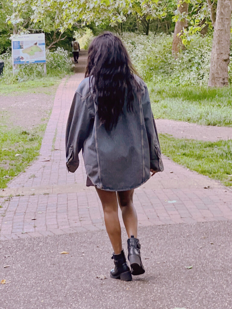 Woman walking in park pavement wearing denim jeans coat with ankle boots