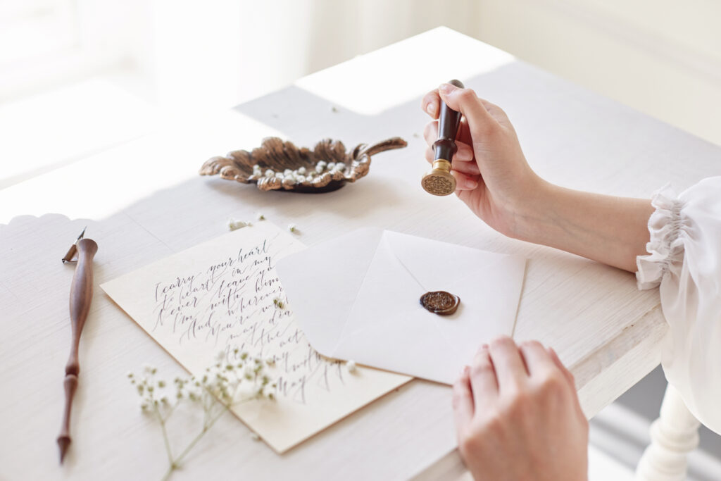 Girl writing a letter to her loved one sitting at the table in a white light dress. White flowers next to her on the table