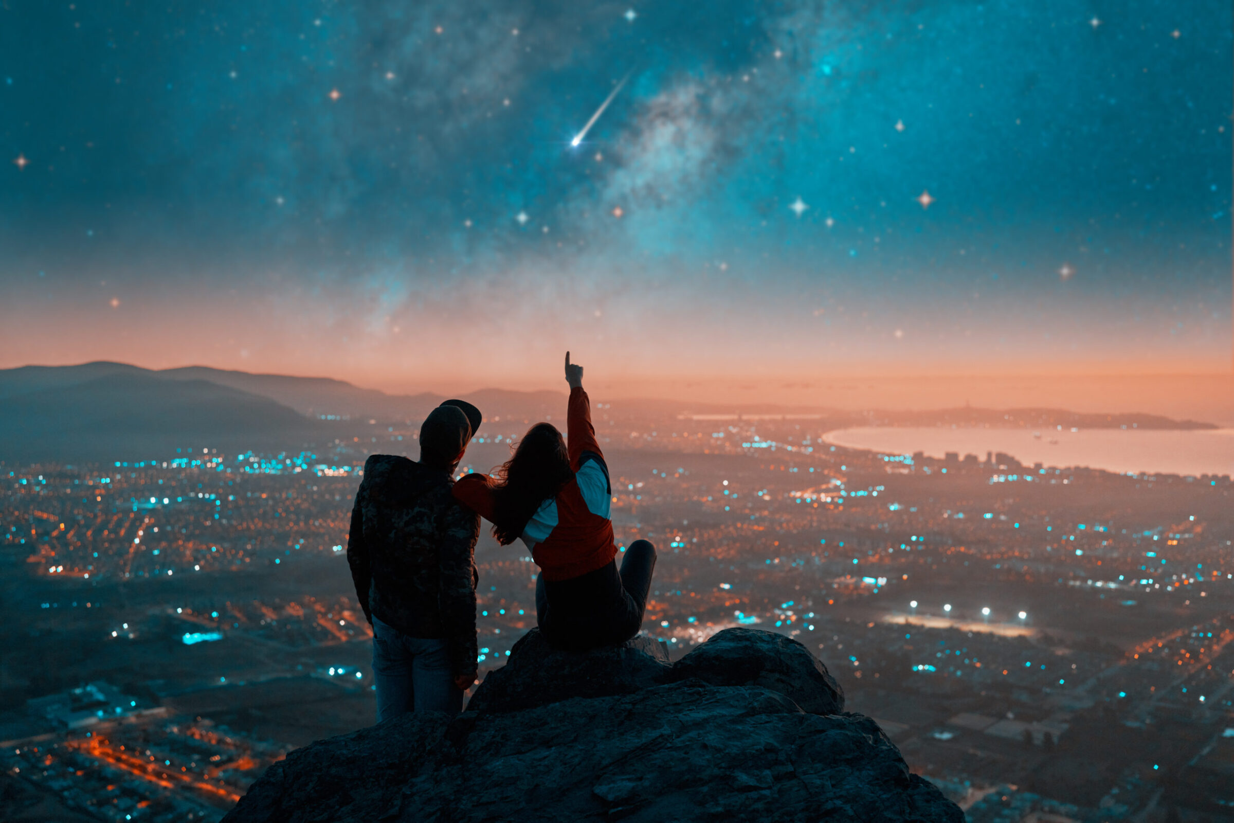 Man and woman sitting on a rock star gazing at night. Woman pointing to the sky