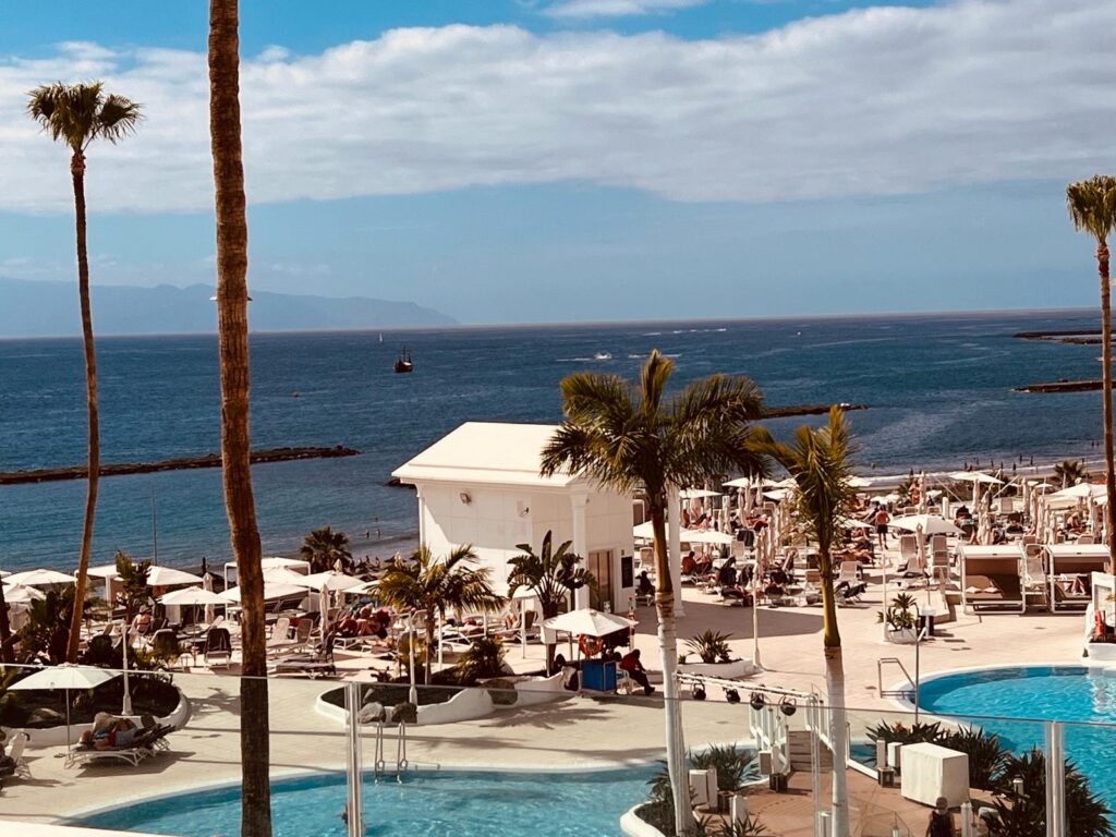 Going On Holiday Abroad? A picture by Chic Chui of a seaside resort with sunbeds, sparkling blue sea, and poolside.