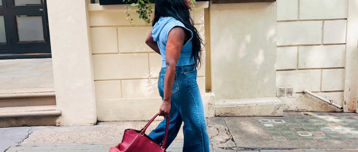 Woman wearing a blue denim outfit and carrying a red handbag while walking along a London street.