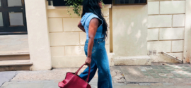 Woman wearing a blue denim outfit and carrying a red handbag while walking along a London street.