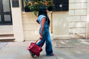 Woman wearing a blue denim outfit and carrying a red handbag while walking along a London street.