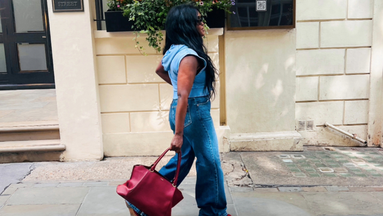 Woman wearing a blue denim outfit and carrying a red handbag while walking along a London street.