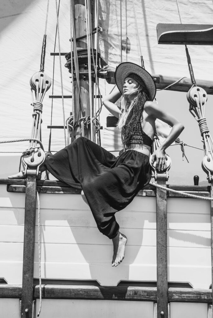 A beautiful woman sitting on the hull of a ship, looking out at the vast ocean, enjoying the sea breeze.