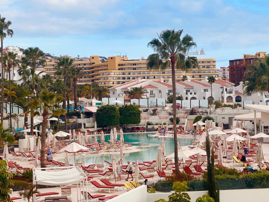 Luxurious poolside and beach resort in Tenerife with palm trees and white modern accommodations.