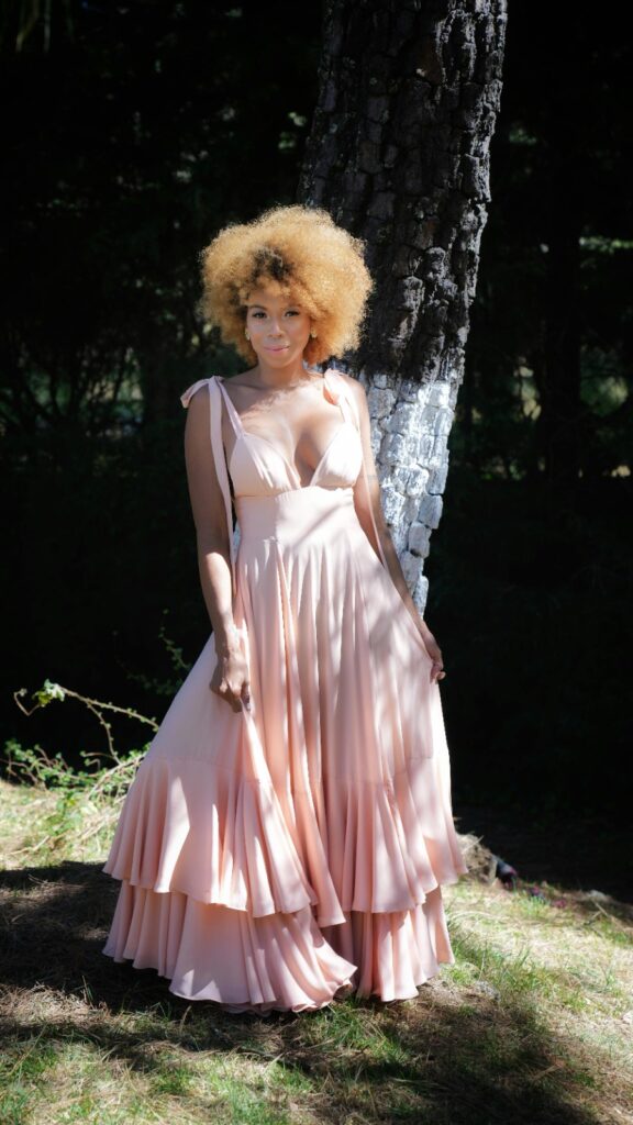 A woman wearing a flowing pastel pink dress with ruffled layers, perfect for summer outfits for an outdoor summer event.