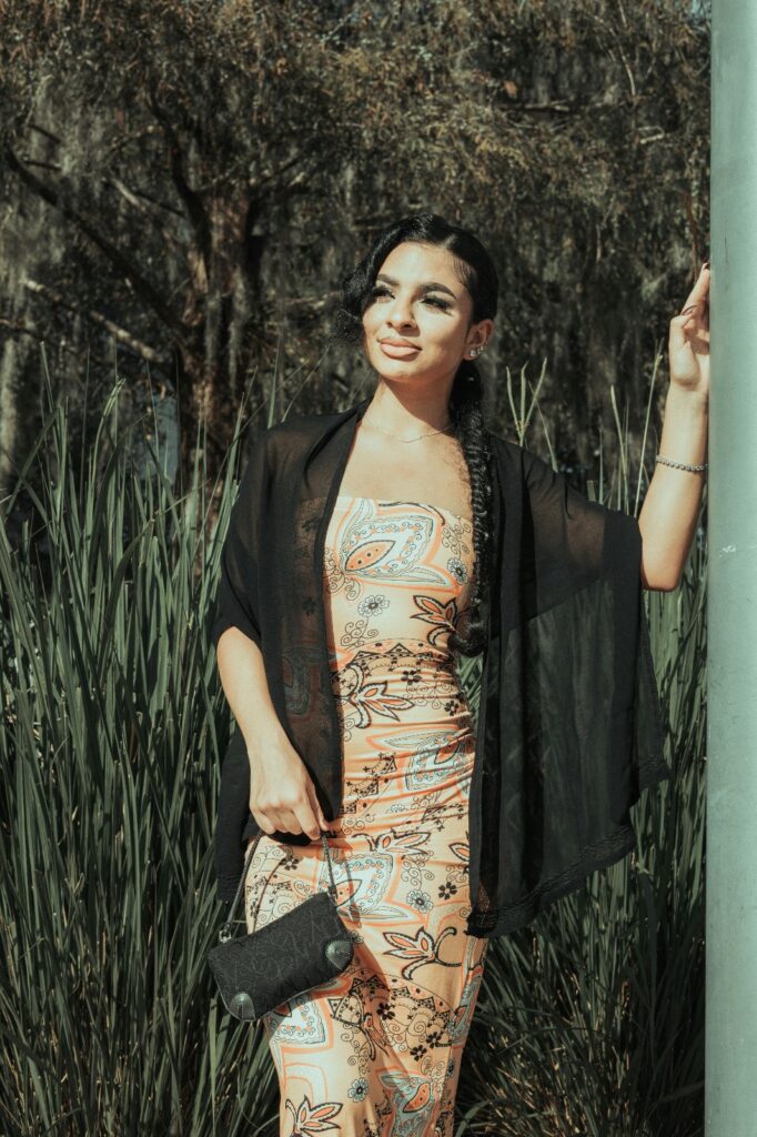 A woman wearing a paisley dress, draping a black sheer shawl around her shoulders, standing outdoors.