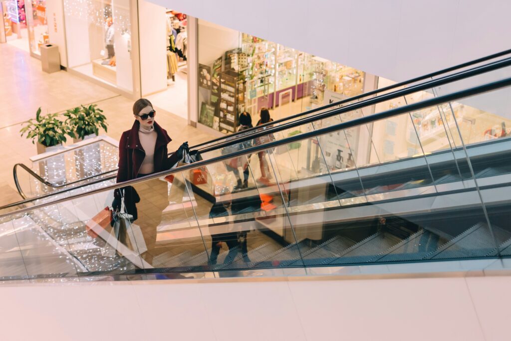 Woman in a mall carrying shopping bags in both hands going up the escalator