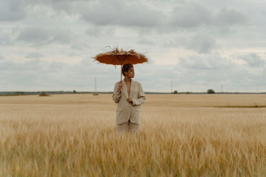 Woman in beige suit holding a straw parasol in a golden wheat field, illustrating a summer fashion mistake.