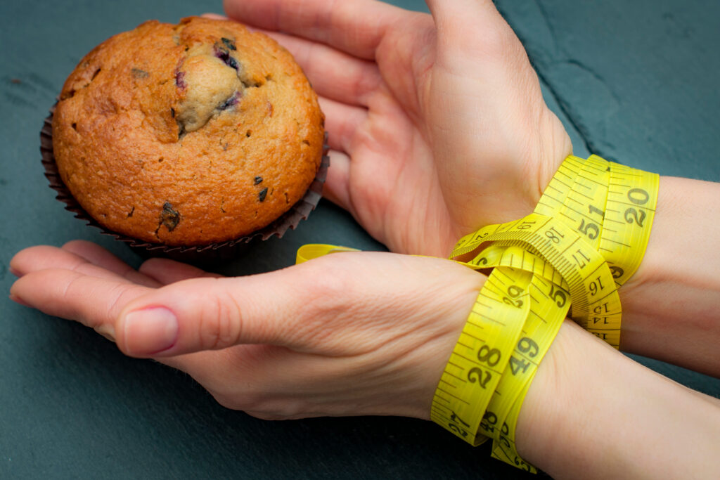 Diet, bondage and delayed gratification concept with woman hand reaching for a muffin while her hands are tied together with measuring tape a symbol of dieting and self control.
