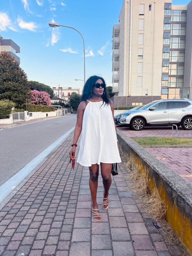 A woman in a cream linen dress walks down a city street.