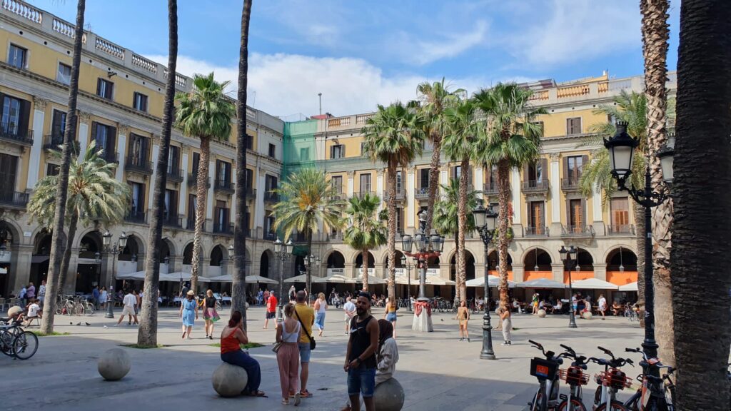 Bustling Plaça Reial in Barcelona, Spain, filled with vibrant cafes and tourists. A perfect spot for a September holiday