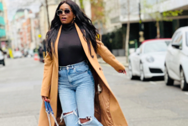Stylish Black woman walking confidently down a city street wearing a camel coat, black turtleneck, and ripped jeans – showcasing how fashion choices like bold outerwear and fitted denim can boost mood and motivation.