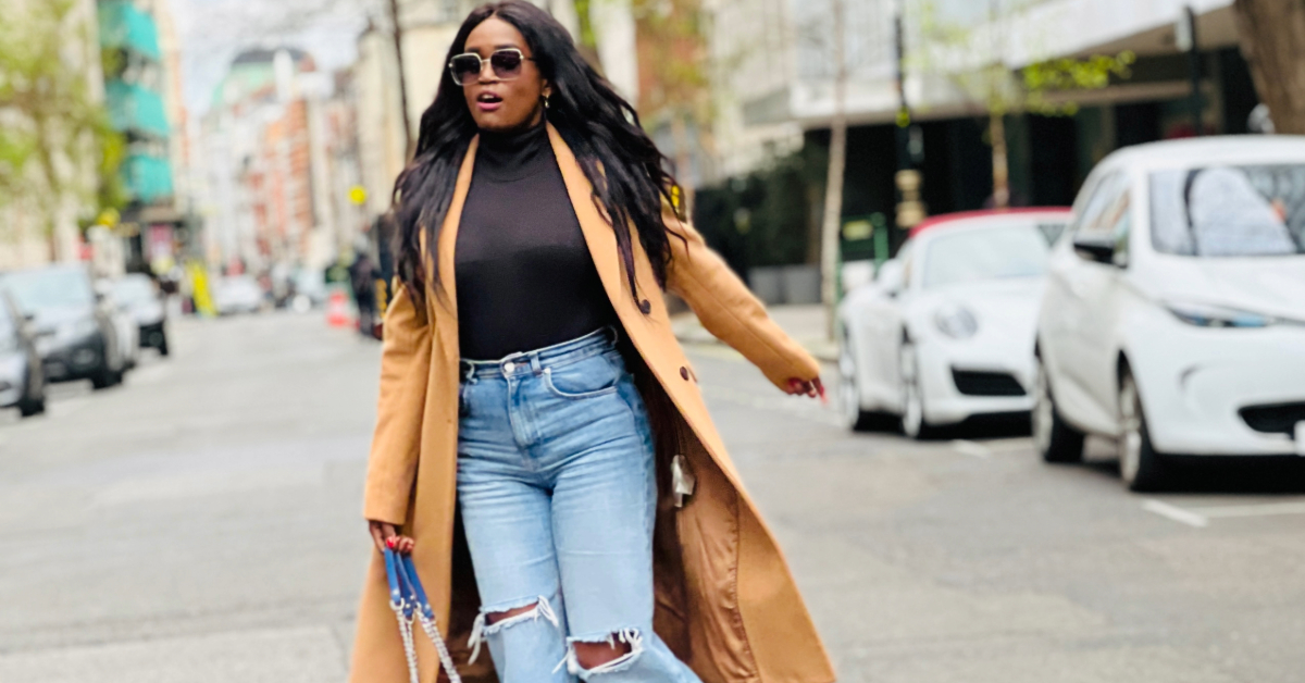 Stylish Black woman walking confidently down a city street wearing a camel coat, black turtleneck, and ripped jeans – showcasing how fashion choices like bold outerwear and fitted denim can boost mood and motivation.
