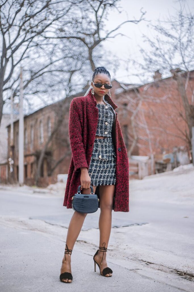 A young woman is strolling down a street, wearing a chic tweed suit from her fall outfits collection. She has accessorised with a black handbag and heeled sandals and sunglasses.