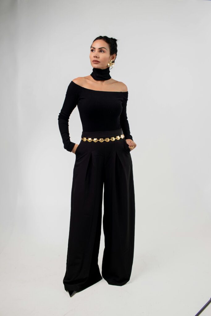 Woman wearing an all-black, off-the-shoulder outfit with gold belt and wide-leg trousers