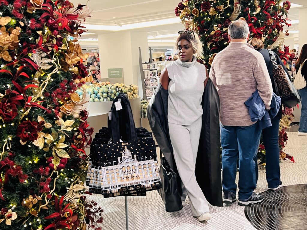 A fashionable woman walking through a festive store with Christmas decorations, symbolising excitement for the upcoming holiday season as a way to cope with seasonal blues.