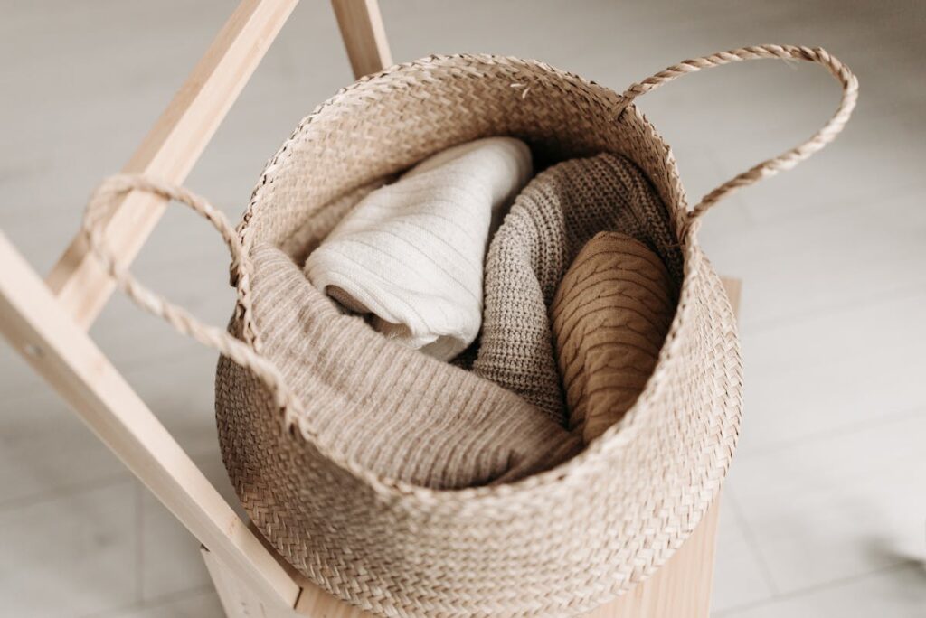 Best Sweaters: A woven basket filled with cozy, neutral-toned fall sweaters featuring ribbed and cable knits.