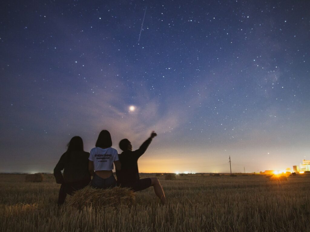 Three people sitting on a rock looking at the stars at night. One of the top travel trends that's gaining traction amongst travellers