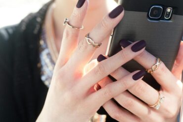 person with black nail polish holding a phone