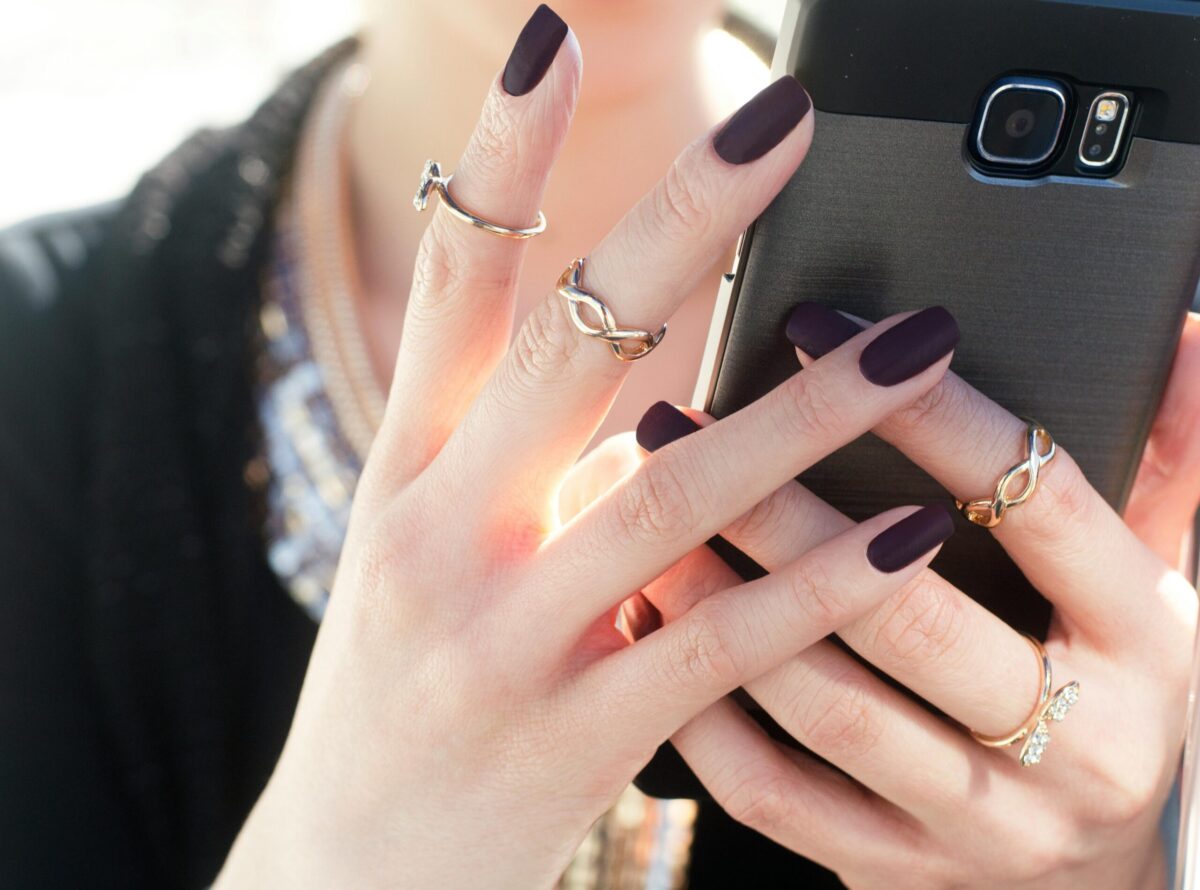 person with black nail polish holding a phone
