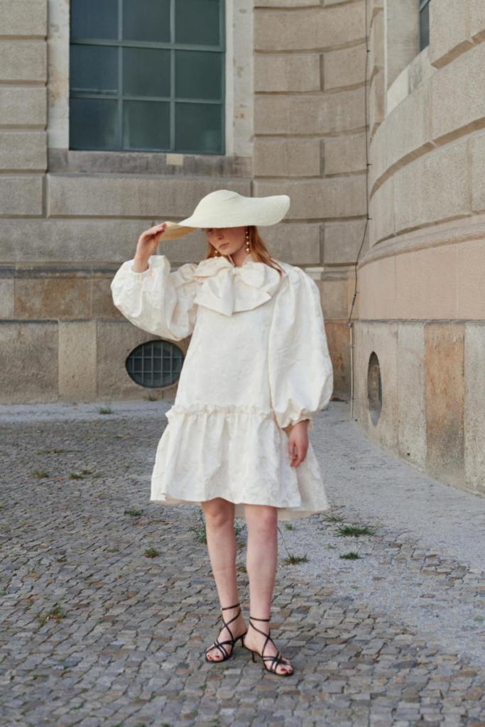 Woman in a white airy poplin dress, wide-brimmed hat, and sandals, embodying stylish summer outfits with a minimal, effortless look.