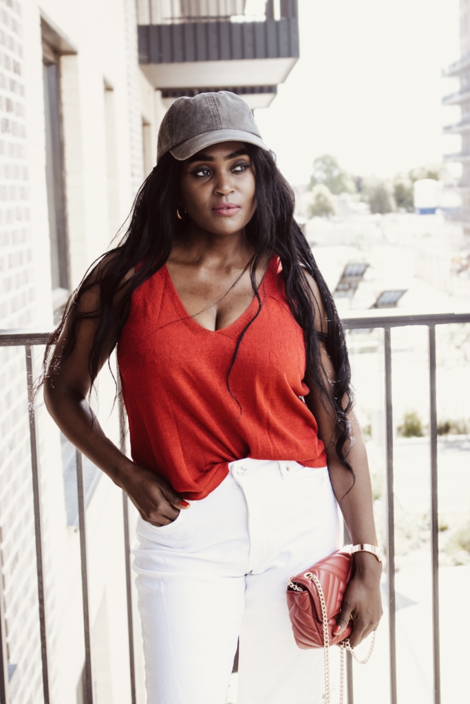 Woman in a cherry-red top and white jeans with a red handbag