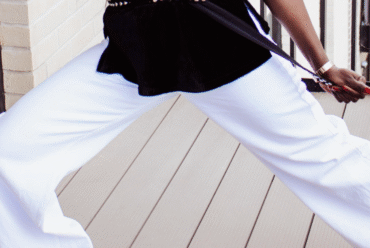 Close-up of a woman's legs in white wide-leg pants on a light wooden floor.