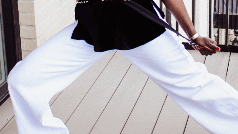 Close-up of a woman's legs in white wide-leg pants on a light wooden floor.