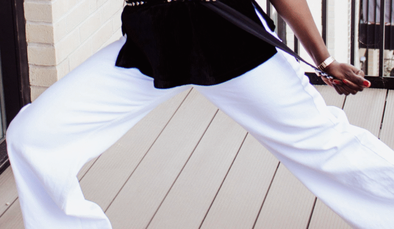 Close-up of a woman's legs in white wide-leg pants on a light wooden floor.