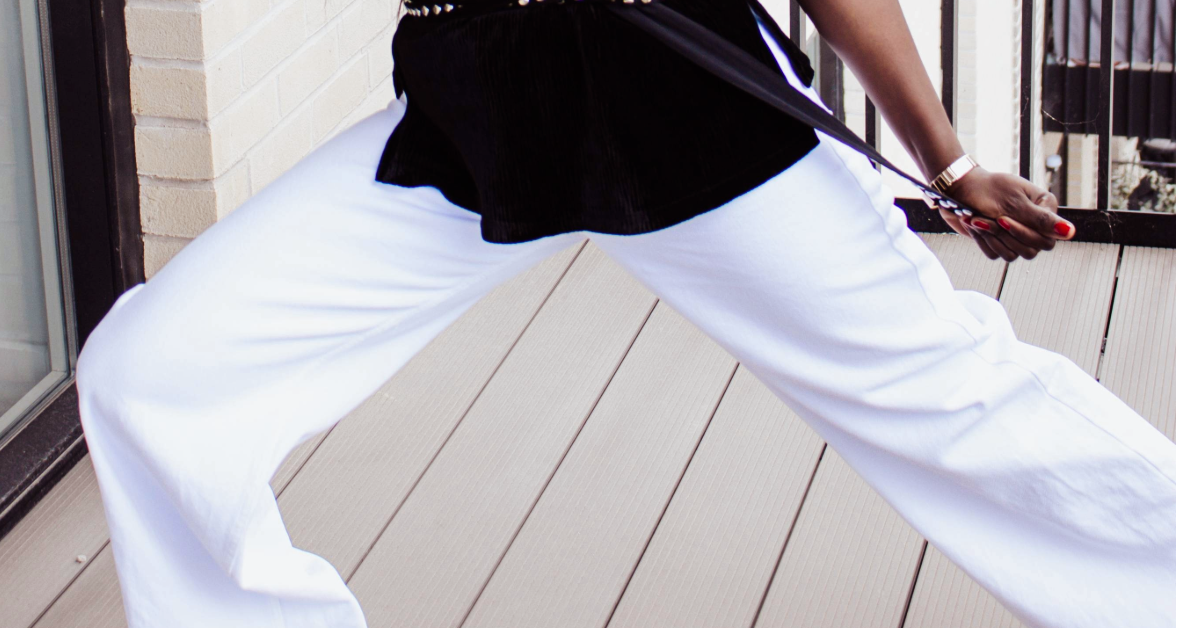 Close-up of a woman's legs in white wide-leg pants on a light wooden floor.