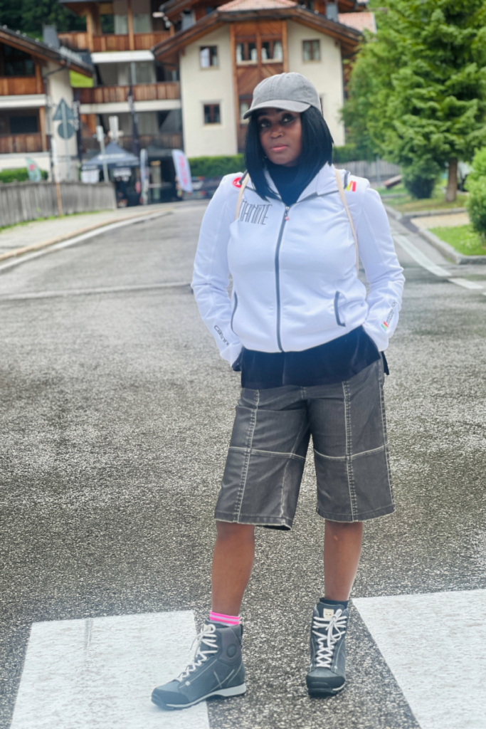 Woman in a white jumper, shorts, and hiking boots standing in Corvara, Italy — highlighting one of the reasons to visit Corvara in summer.